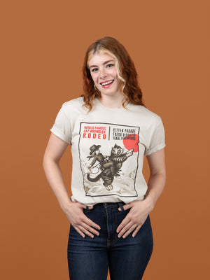 Woman wearing a Cat Wrangler Rodeo T-shirt in front of a brown background