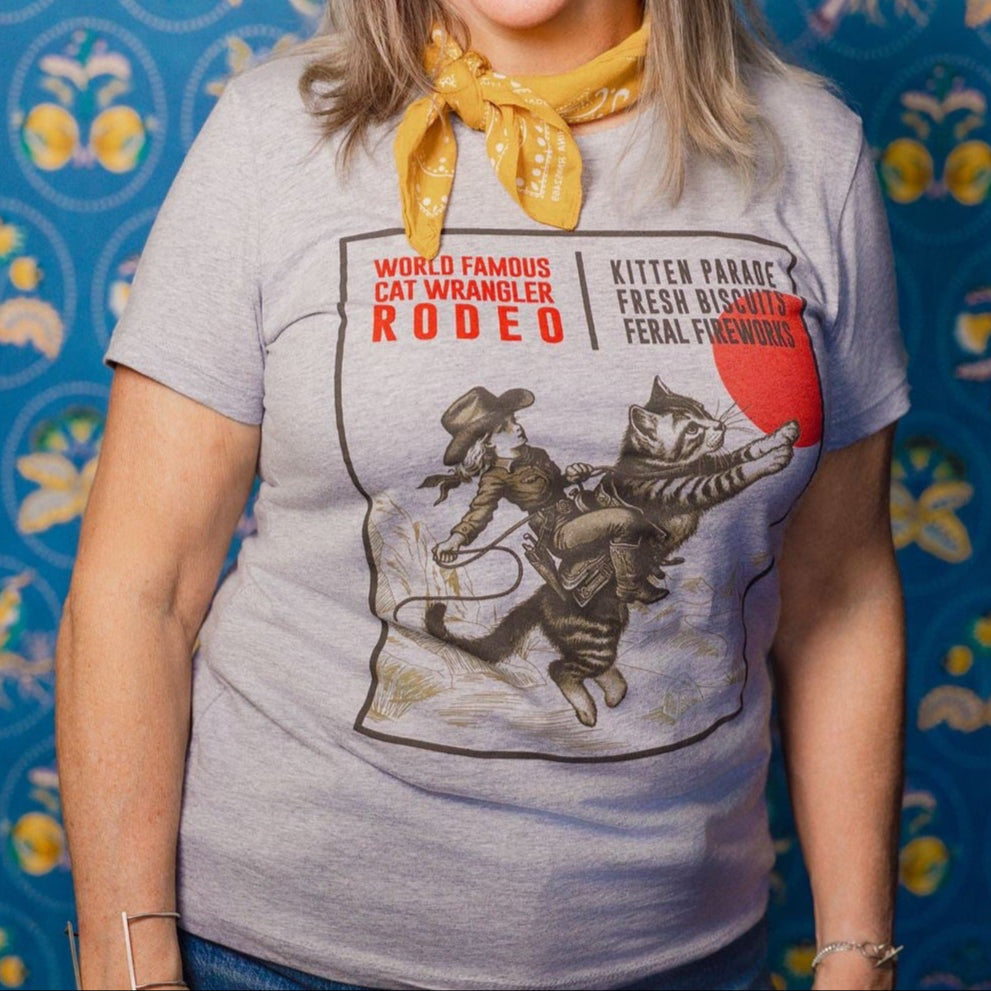 Close up image of a Woman wearing a Cat Wrangler Rodeo tee against a patterned background