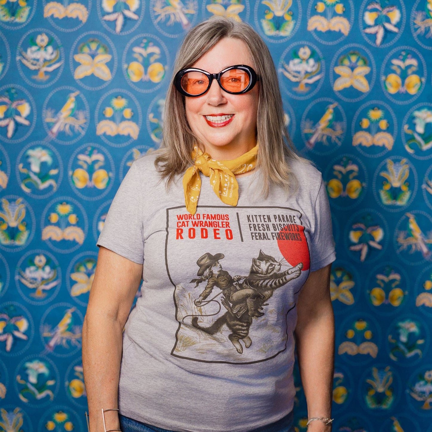 Woman wearing a Cat Wrangler Rodeo tee against a patterned background