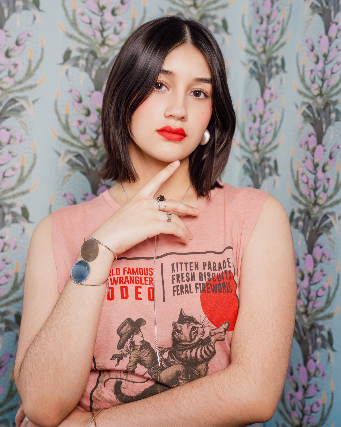 Woman wearing a pink cat wrangler tank top in front of patterned wallpaper