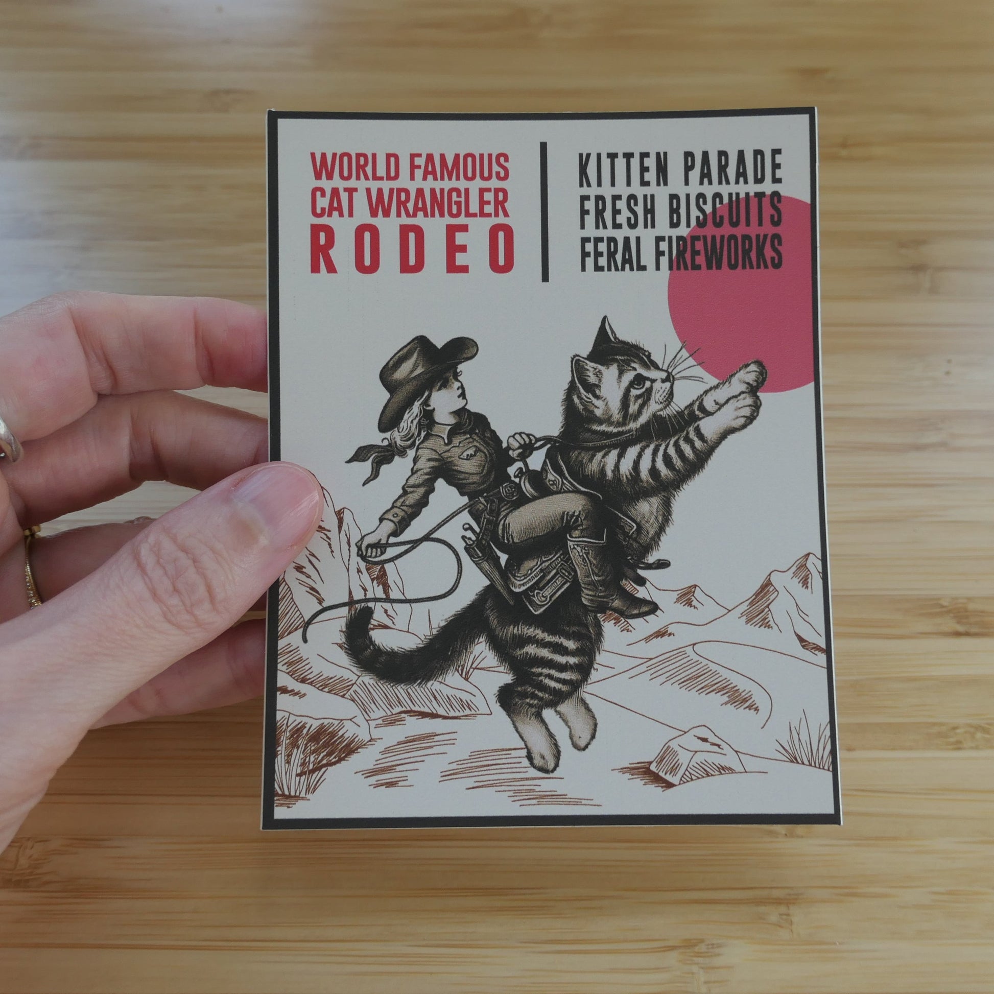 Hand holding a Cat Wrangler Rodeo sticker