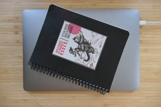 Cat Wrangler Sticker on a black notebook sitting on a laptop computer