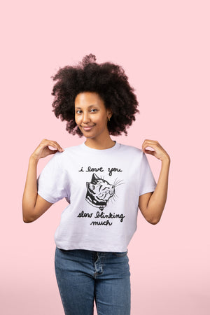 Woman wearing a lavender t-shirt with a graphic of a cat and text, standing against a pink background
