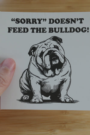 Someone holding a sticker that says Sorry Doesn't Feed the Bulldog with an image of a bulldog in black and white