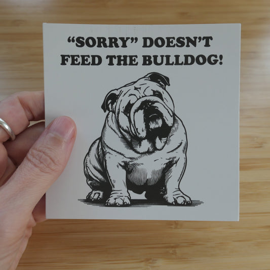 Someone holding a sticker that says Sorry Doesn't Feed the Bulldog with an image of a bulldog in black and white