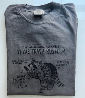 Folded grey Comfort Colors t-shirt with hand drawn art of a cute and funny raccoon