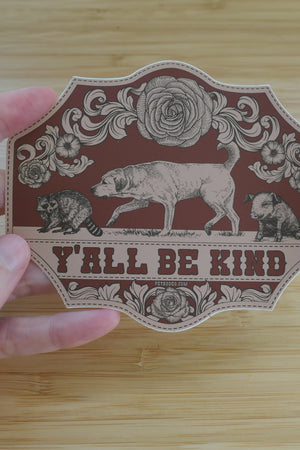 A 4 inch, die-cut vinyl sticker that says Ya'll Be Kind with illustrations of a dog, raccoon, and piglet