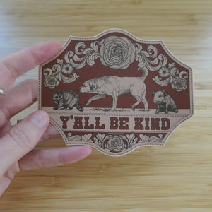 A 4 inch, die-cut vinyl sticker that says Ya'll Be Kind with illustrations of a dog, raccoon, and piglet