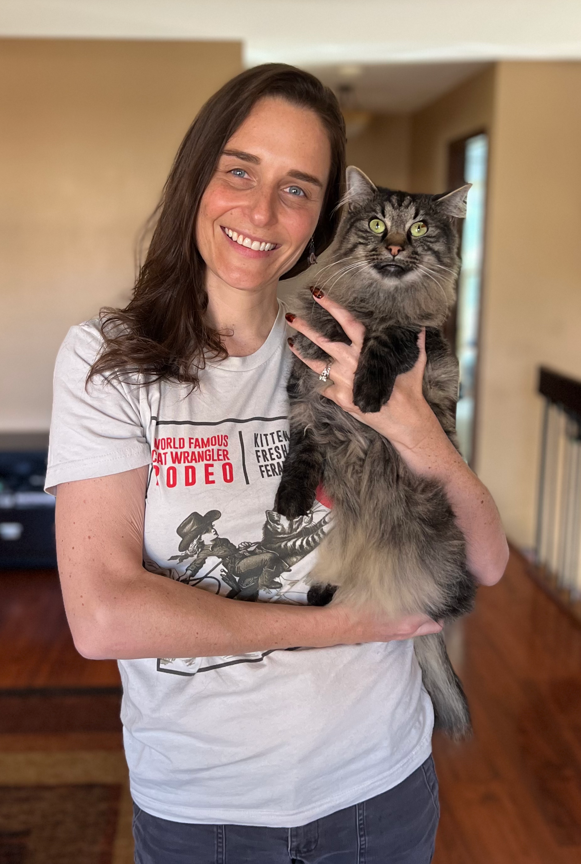 Woman holding her pet cat and wearing a Cat Wrangler Rodeo graphic tee